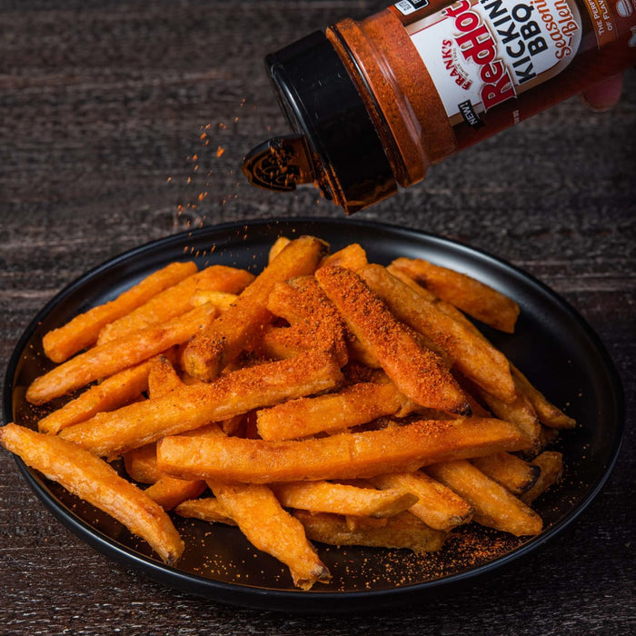 A plate of sweet potato fries are being sprinkled with Franks RedHot Kickin BBQ Seasoning.