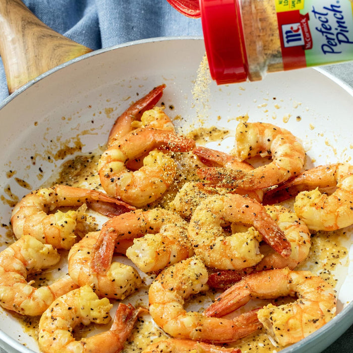 A white pan with cooked shrimp being seasoned with McCormick Perfect Pinch seasoning.