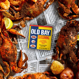 A can of Old Bay seasoning sits on a table with a spread of crab legs and potatoes.