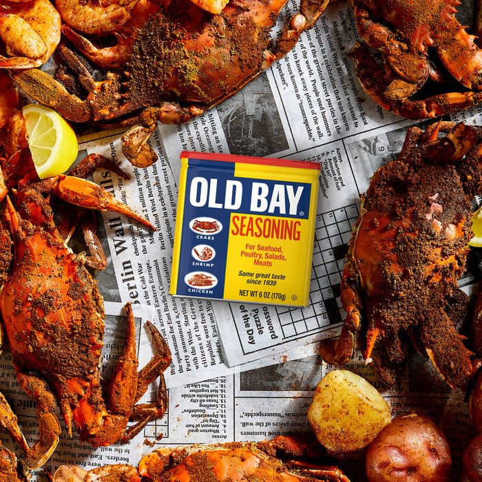 A can of Old Bay seasoning sits on a table with a spread of crab legs and potatoes.
