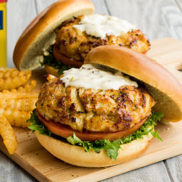 Two crab cakes on buns with lettuce, tomato, and a creamy sauce.