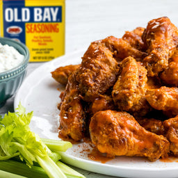 A plate of Old Bay seasoned chicken wings with celery sticks and a bowl of ranch dressing.