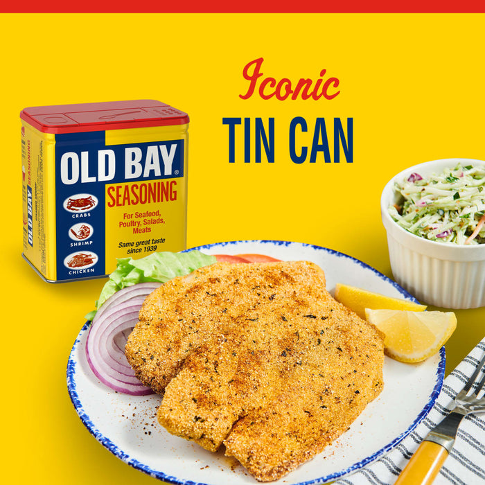 A can of Old Bay Seasoning next to a plate of fried fish with lemon wedges and red onion, and a bowl of coleslaw.