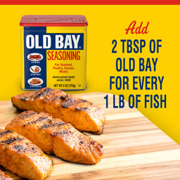 A container of Old Bay seasoning with grilled fish on a cutting board.
