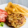 A golden brown crab cake prepared with Old Bay Regular Crab Cake Seasoning Mix 1.24 Oz served on a plate with crinkle cut fries and a fresh tomato slice.