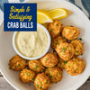 A white bowl filled with golden brown crab balls seasoned with Old Bay Regular Crab Cake Seasoning Mix 1.24 Oz and served with a side of creamy dipping sauce and lemon wedges.
