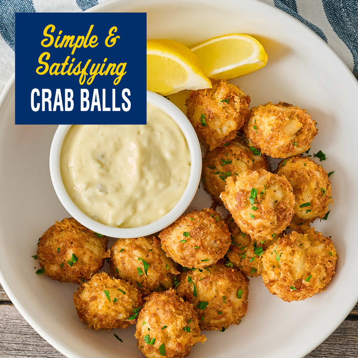 A white bowl filled with golden brown crab balls seasoned with Old Bay Regular Crab Cake Seasoning Mix 1.24 Oz and served with a side of creamy dipping sauce and lemon wedges.