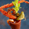 A bloody mary garnished with a crab leg bacon celery a pickle a lemon wedge and a shrimp.