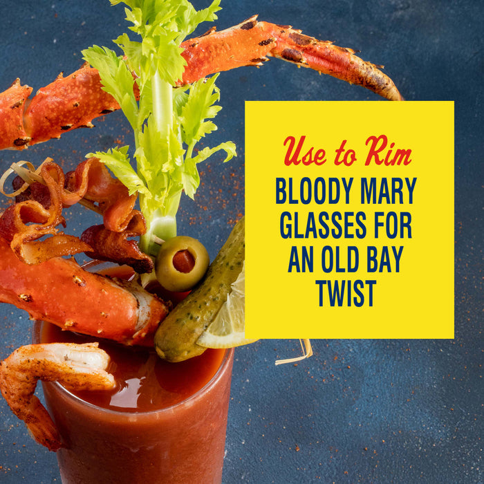 A Bloody Mary garnished with crab legs bacon celery olives a pickle and a shrimp with a yellow box that says Use to Rim Bloody Mary Glasses for an Old Bay Twist.