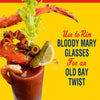 A Bloody Mary garnished with crab legs bacon celery olives a pickle and a lemon wedge with text that says Use to rim Bloody Mary glasses for an Old Bay twist.