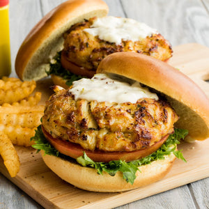 Two crab cakes on buns with lettuce, tomato, and a creamy sauce.