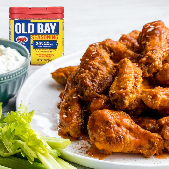 A plate of buffalo wings with celery sticks and a container of Old Bay Seasoning.