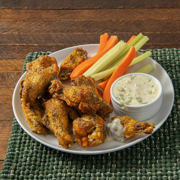 A plate of crispy chicken wings with celery sticks carrots and blue cheese dip.