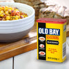 A container of Old Bay Seasoning is displayed next to a bowl of corn salsa and grilled food.