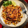 A plate of grilled fish served over corn salsa with a lime wedge and cilantro garnish.
