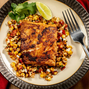 A plate of grilled fish served over corn salsa with a lime wedge and cilantro garnish.