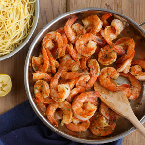 A pan of sauteed shrimp with pasta and a lemon wedge, suggesting a delicious and easy meal.