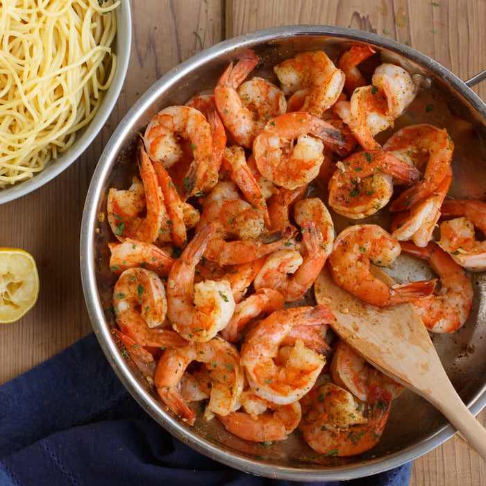 A pan of sauteed shrimp with pasta and a lemon wedge, suggesting a delicious and easy meal.