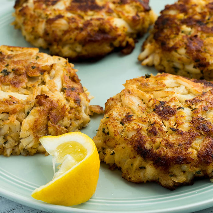 A plate of golden-brown crab cakes is served with a lemon wedge.