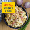 A bowl of Old Bay potato salad with garlic and herbs is displayed with red onions and chives.