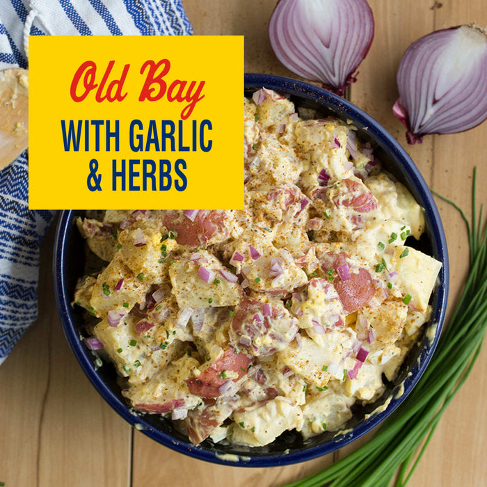 A bowl of Old Bay potato salad with garlic and herbs is displayed with red onions and chives.
