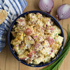 A bowl of creamy potato salad with red potatoes, eggs, and red onion, garnished with chives.