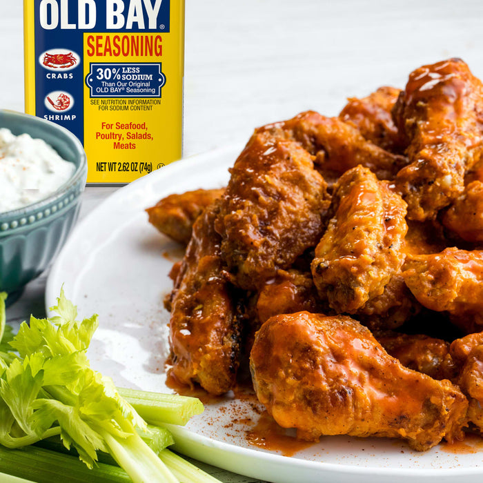A plate of Old Bay seasoned chicken wings is served with celery sticks and a side of dip.