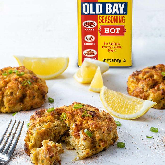 A box of Old Bay Hot Seasoning is displayed behind crab cakes garnished with lemon wedges and green onions.