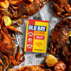 A can of Old Bay Hot Seasoning is surrounded by cooked crabs and potatoes, suggesting its use in seafood boils.