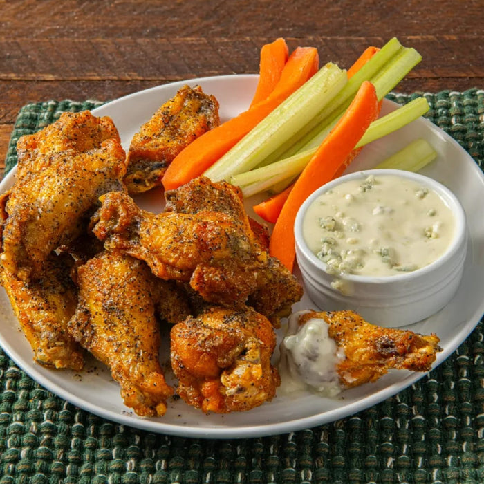 A plate of seasoned chicken wings is served with carrot and celery sticks, alongside a creamy dipping sauce.
