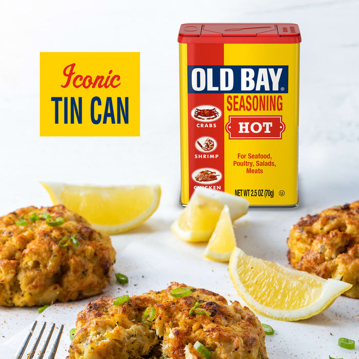 A can of Old Bay Hot Seasoning is displayed with crab cakes and lemon wedges.