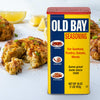 A container of Old Bay Seasoning with crab cakes in the background.