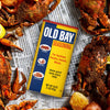 A can of Old Bay seasoning sits on top of a newspaper with crab legs and potatoes.