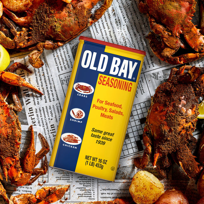 A can of Old Bay seasoning sits on top of a newspaper with crab legs and potatoes.