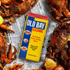 A can of Old Bay seasoning sits on top of a newspaper with crab legs and potatoes.