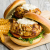 Two crab cake sandwiches with lettuce, tomato, and a creamy sauce on a wooden cutting board with french fries.