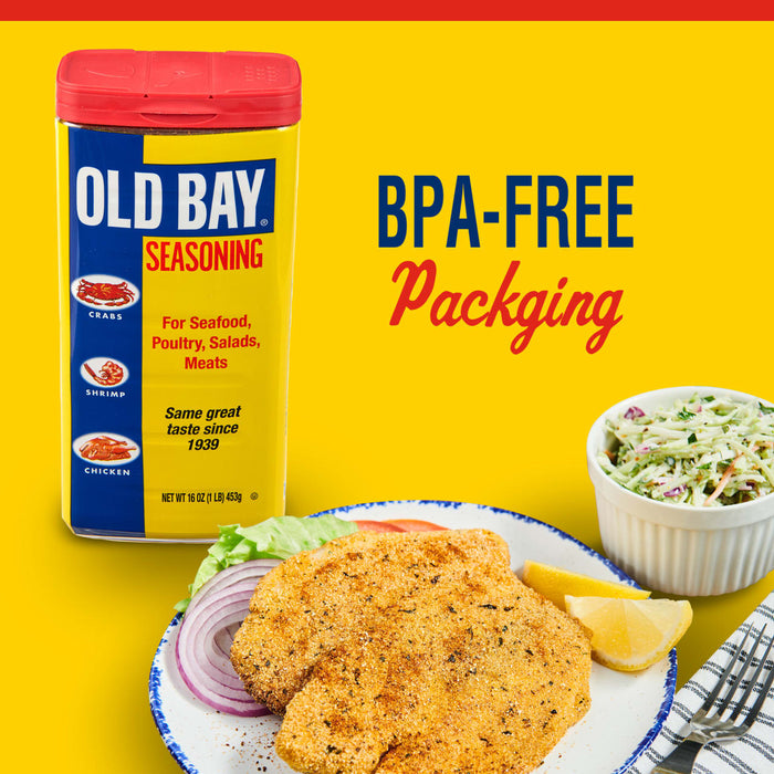 A container of Old Bay Seasoning next to a plate of fried fish, lemon wedges, and red onion with a bowl of coleslaw and a fork.