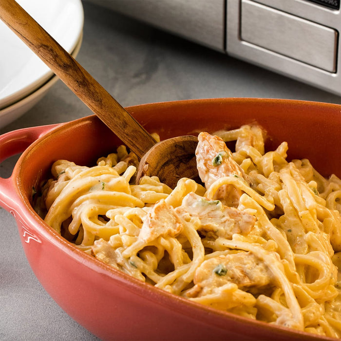 A close up of a bowl of creamy chicken pasta with a wooden spoon.