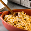 A close up of a bowl of creamy chicken pasta with a wooden spoon.