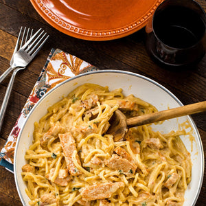 A close-up of a creamy pasta dish with chicken and a wooden spoon.