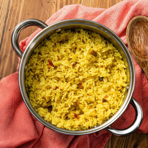 A pot of vibrant yellow rice sits on a wooden surface with a pink cloth, suggesting a flavorful and comforting meal.