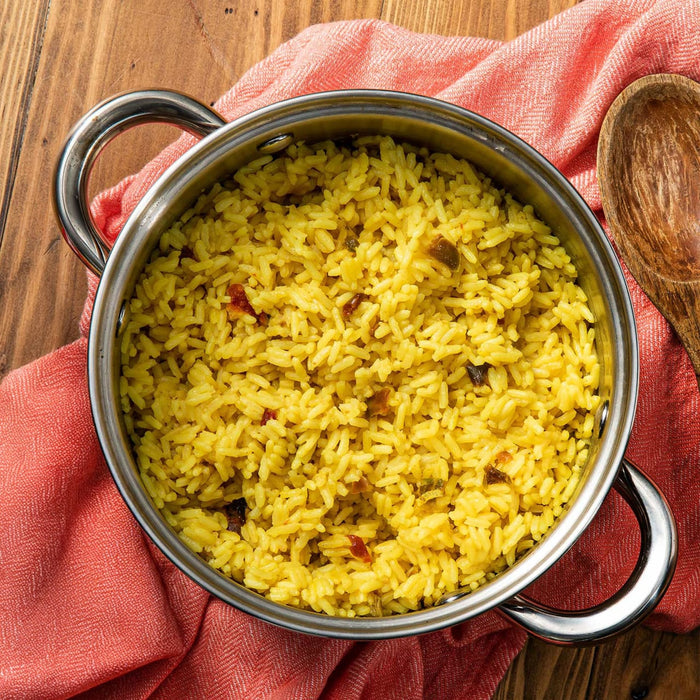 A pot of vibrant yellow rice sits on a wooden surface with a pink cloth, suggesting a flavorful and comforting meal.