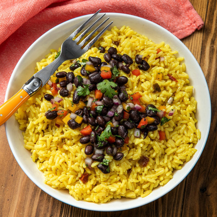 A vibrant bowl of yellow rice topped with black beans, peppers, and cilantro, served with a fork.