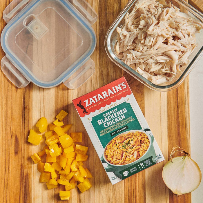 A box of Zatarain's Creamy Blackened Chicken with a serving suggestion of the dish, a container of shredded chicken, chopped yellow bell peppers, and a whole onion.