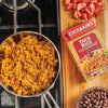 A pot of Zatarain's Taco Rice on a stovetop next to a box of Zatarain's Taco Rice and a bowl of black beans.