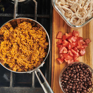 A close-up of a pot of rice, a bowl of black beans, chopped tomatoes, and shredded chicken.