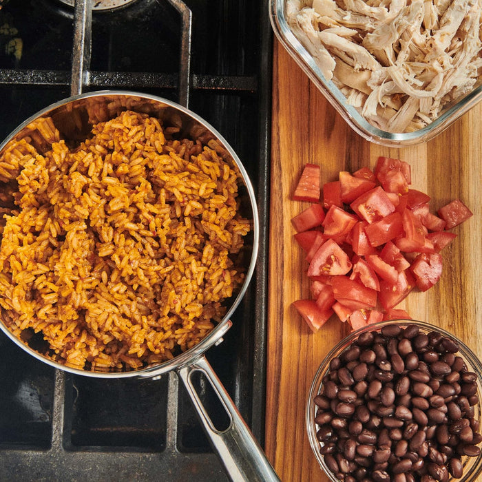 A close-up of a pot of rice, a bowl of black beans, chopped tomatoes, and shredded chicken.