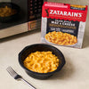 A box of Zatarain's Cajun-Style Mac &amp; Cheese sits next to a microwave and a bowl of the prepared mac and cheese with a fork.