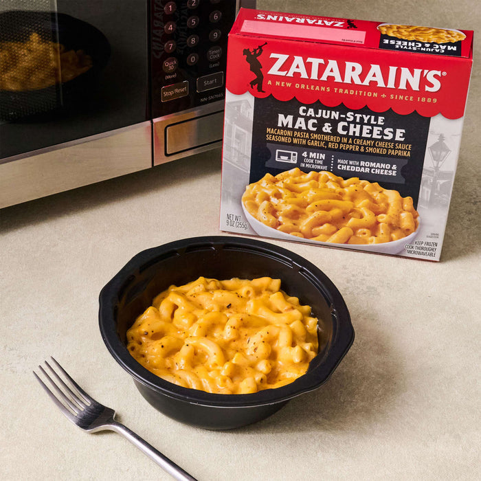 A box of Zatarain's Cajun-Style Mac &amp; Cheese sits next to a microwave and a bowl of the prepared mac and cheese with a fork.