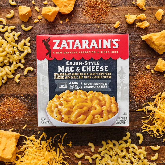 A box of Zatarain's Cajun-Style Mac &amp; Cheese is surrounded by macaroni, cheese chunks, shredded cheese, and spices on a wooden surface.